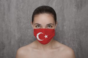 תרגום מעברית לטורקית בתמונה: אישה מכסה את הפה במסכה בצבעי דגל טורקיה 