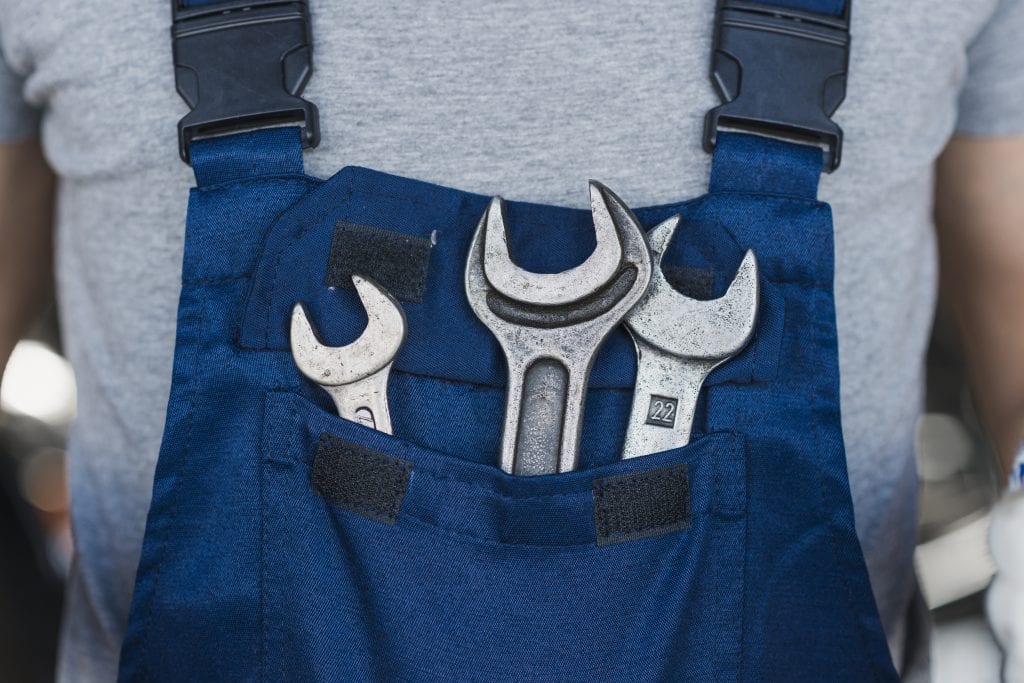 תרגום טכני בתמונה: מכונאי לובש סרבל כחול ועליו תלויים שלוש מפתחות שוודים 