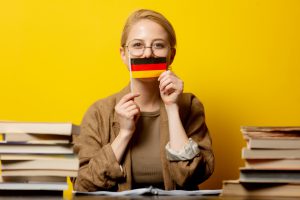 תרגום לגרמנית - בתמונה מתרגמת לגרמנית מחזיקה דגל גרמניה בין שתי ערמות ספרים 