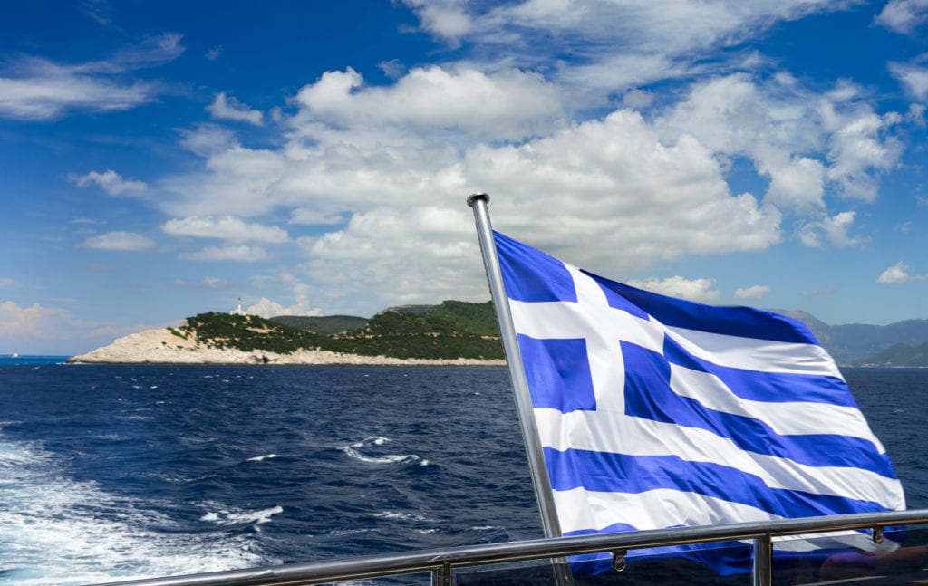 דגל יוון מתנפנף על סירה על רקע אי וים כחול